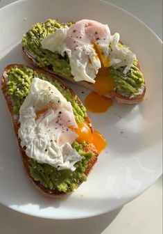 two pieces of bread with eggs and avocado on them sitting on a plate