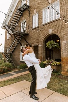 a bride and groom pose for a photo in front of a brick building with stairs