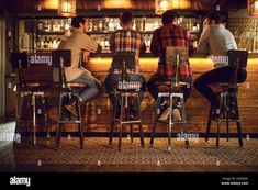 three people sitting at a bar with their backs turned to the camera - stock image