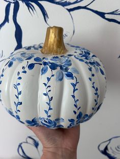 a blue and white painted pumpkin being held in front of a wallpapered background