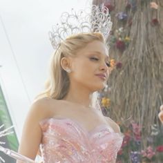 a woman in a pink dress standing next to a man wearing a tiara and holding an umbrella