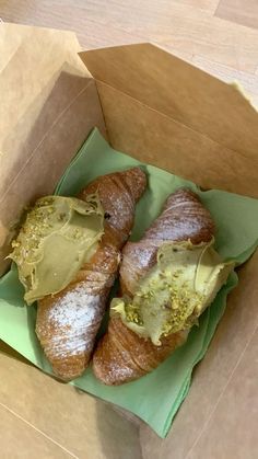 three croissants in a box with powdered sugar and green icing