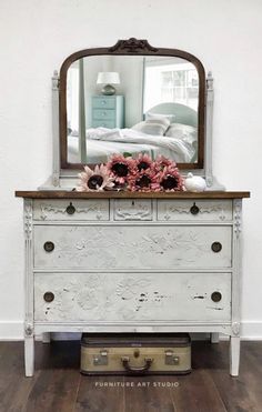 a white dresser with flowers and a mirror on top