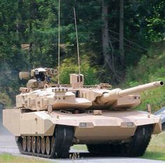 a tank driving down a road next to a lush green forest on a sunny day