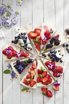 a pie with fruit on it sitting on top of a white table next to flowers