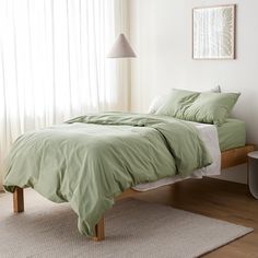 a bed with green sheets and pillows in a white room next to a large window