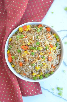 a white bowl filled with rice and veggies on top of a red napkin