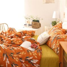 a bed with an orange comforter and two pillows on top of it next to a table