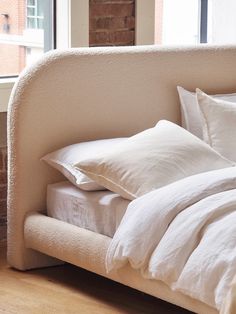 a bed with white linens and pillows in front of a window