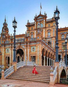 a woman in a red dress is standing on the steps outside an old building with ornate architecture