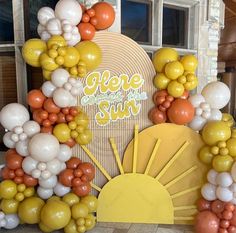 an arch made out of balloons with the words here comes sun on it