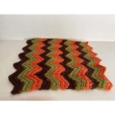 a crocheted rug with an orange, brown and green zigzag pattern