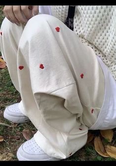 a person sitting on the ground with their legs crossed wearing white sweatpants and red hearts