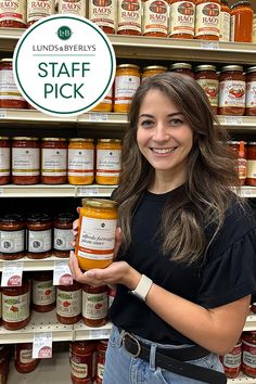 a woman holding up a jar of honey in front of shelves full of jams