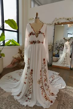 a white dress on display in front of a large window with plants growing out of it