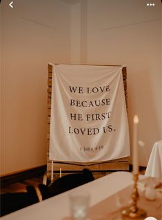 a white banner with the words we love because he first loved us on it next to candles