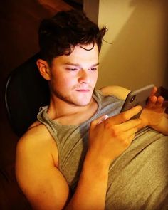 a young man sitting in a chair looking at his cell phone while holding it up to his chest