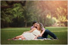 a man and woman sitting on top of a grass covered field next to each other