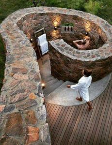 an outdoor hot tub surrounded by stone walls and wooden decking, with lights on the side