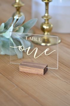 a clear acrylic sign sitting on top of a wooden table next to a candle holder