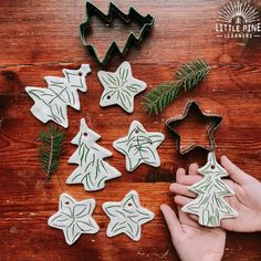 someone is making christmas cookies with cookie cutters on a wooden table next to them