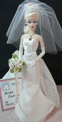 a barbie doll dressed in a wedding dress and veil holding a bridal flash card