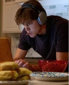 a young man wearing headphones looking at a laptop computer with food in front of him