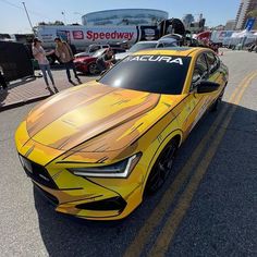 a yellow sports car is parked on the side of the road in front of some people