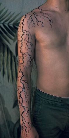 a man with a lightning tattoo on his left arm and chest is standing in front of a palm tree