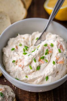 a bowl filled with cream cheese and topped with green onions next to sliced lemons