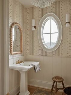 a white sink sitting under a round window next to a wooden table and chair in a bathroom