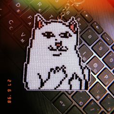 a cross stitch cat sitting on top of a computer keyboard