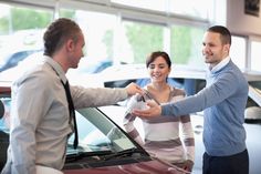 two men and a woman shaking hands in front of a car