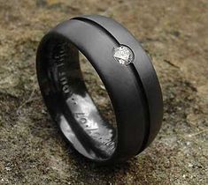 a black wedding ring with a diamond in the center on top of a stone surface