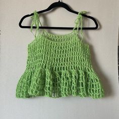 a green crocheted top hanging on a hanger next to a white wall