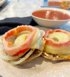 two sandwiches with meat and cheese are on a plate next to a bowl of sauce