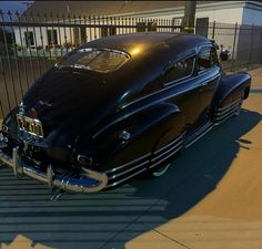 an old black car parked in front of a gated driveway with the sun shining on it