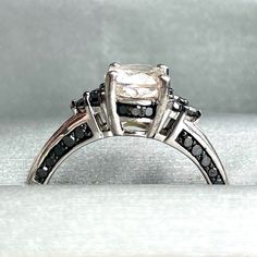 an engagement ring with black and white diamonds on it's sides, sitting on a silver surface