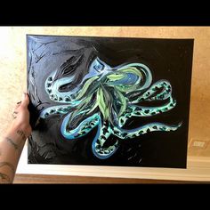 an octopus painting is being held up by a person's hand in front of it