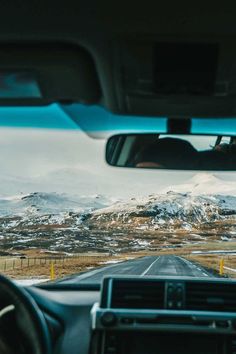 the view from inside a car looking at mountains and snow covered hills in the distance