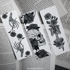 three bookmarks with skulls and roses on them are laying next to an open book