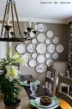 a dining room table with plates on the wall and flowers in vases next to it