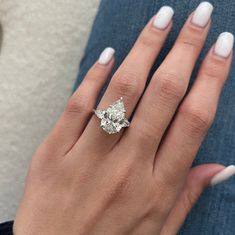 a woman's hand with white nails and a ring on her finger, holding an engagement ring