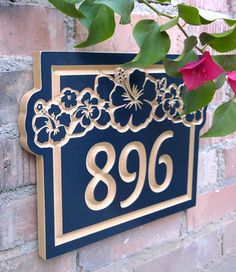 a blue and gold house number sign on a brick wall with flowers in the background