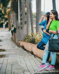 two young women standing next to each other on the sidewalk with their hands in their pockets