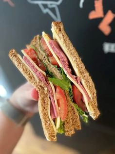 a hand holding a sandwich with meat, lettuce and tomato on toasted bread