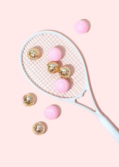 a tennis racket with pink and gold balls coming out of it on a pink background