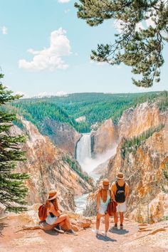 two people sitting on the edge of a cliff overlooking a river and waterfall in yellowstone national park