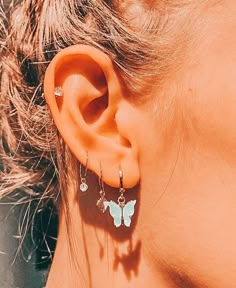 a close up of a person's ear with butterfly shaped earrings on top of it