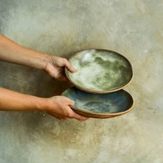 a person holding two plates on top of each other in front of a cement wall